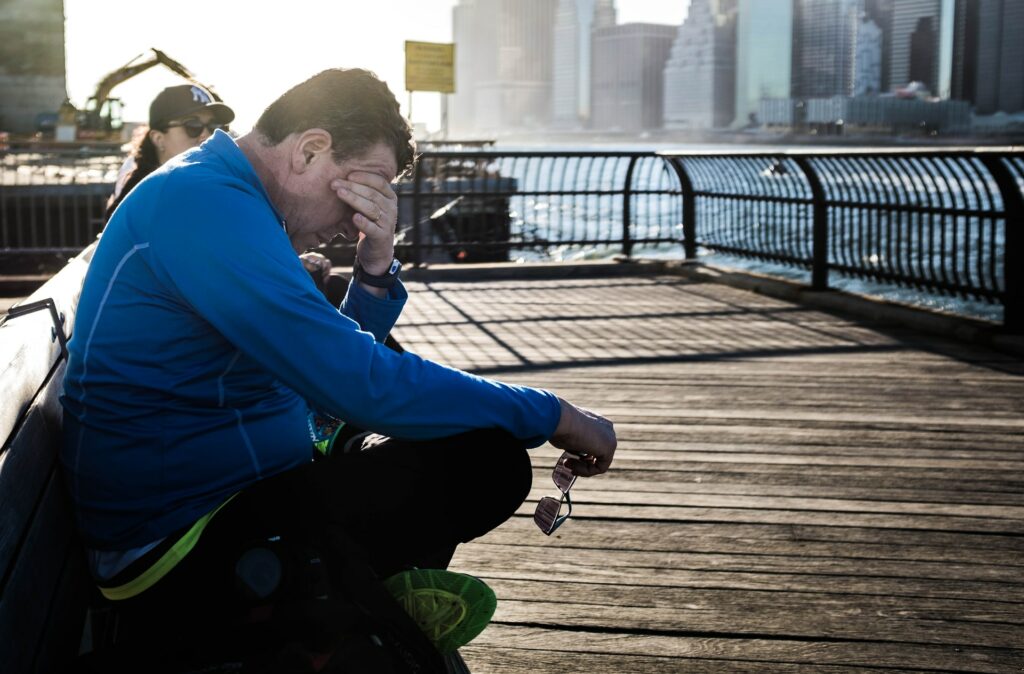 Man on a bench rubbing his eyes due to exhaustion