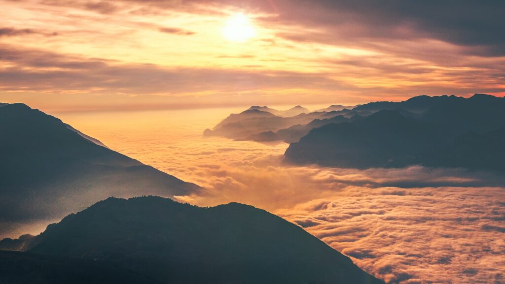 Top of a mountain view with the clouds below and sun in the sky.