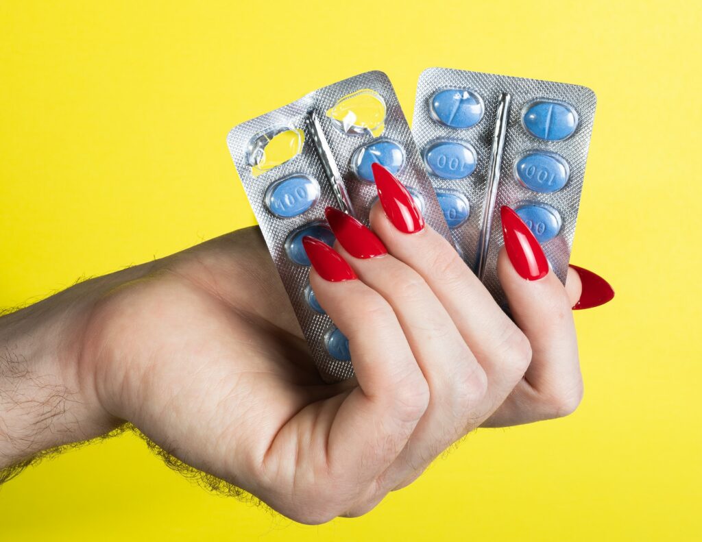 A womans hand holding packets of blue pills.